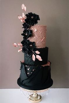 a three tiered black and pink wedding cake with flowers on the top, sitting on a gold pedestal