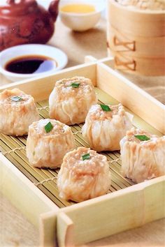 some dumplings are sitting in a wooden tray on a table with dipping sauces