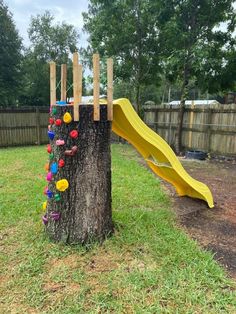 a tree stump with a yellow slide in the middle and colorful balls on it's side