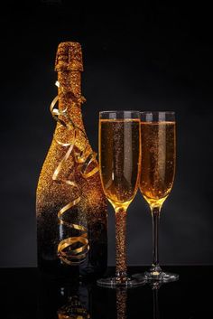 two champagne flutes and a bottle of champagne on a black background with gold streamers