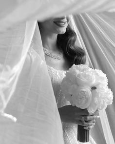 a woman in a white dress holding a bouquet of flowers under a sheer fabric curtain