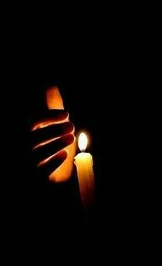 a person holding a lit candle in the dark with their hand on top of it