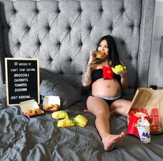 a pregnant woman sitting on a bed eating food and holding a drink in her hand