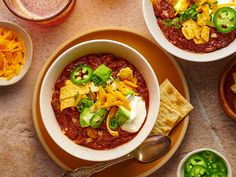 three bowls of chili with cheese, sour cream and tortilla chips on the side