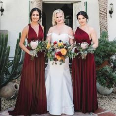 three bridesmaids standing in front of a house holding bouquets and smiling at the camera