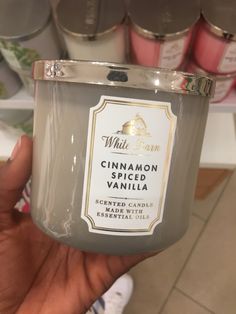 a hand holding a glass jar with cinnamon spiced vanilla on it in front of some candles