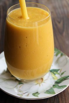 a glass filled with orange juice on top of a white and green plate next to a wooden table