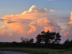 the clouds are pink and orange as the sun sets in the sky over trees on the other side