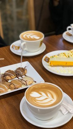 there are two cups of coffee on the table with pastries and desserts in front of them