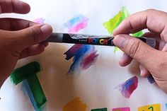 two hands are painting the letters on a piece of paper with colored watercolors