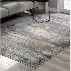 an area rug with grey and gold tones on the floor in front of a couch