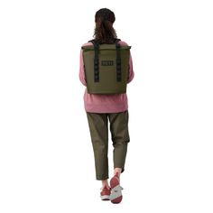 the back view of a woman walking with a green backpack on her back and pink sweater