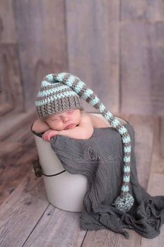 a baby sleeping in a bucket wearing a knitted hat