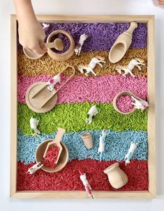 a child's hand reaching for toys in a wooden tray with colored rice on it