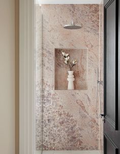 a white vase with flowers in it sitting on a wall next to a shower head