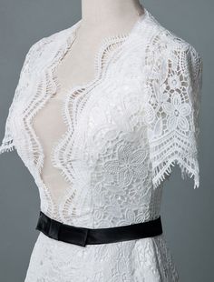 a white lace dress with black belt on mannequin headdress in front of grey background