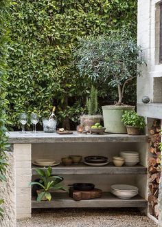 an outdoor kitchen with plants and plates on the counter top, surrounded by greenery