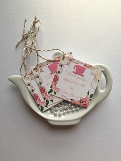 three tags are placed on top of a teapot shaped dish with pearls and twine