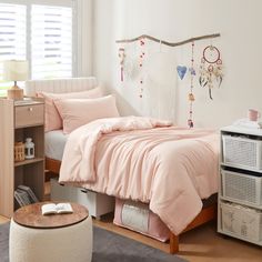 a bed with pink sheets and pillows in a bedroom next to a book shelf on the floor