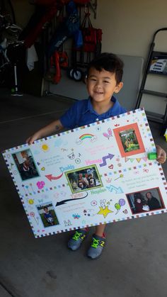 a young boy holding up a large poster with pictures on it's sides and smiling at the camera