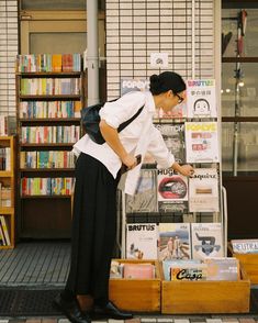 a woman standing next to a stack of books in front of a book store filled with books