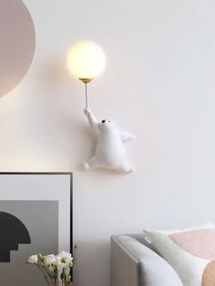 a white bear lamp is on the wall above a gray couch and vase with flowers