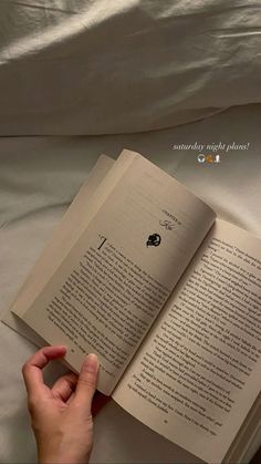 someone is reading a book in bed with their hand on the open book's cover