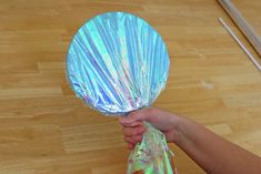 a person holding a plastic wrapped object on top of a hard wood floor with chopsticks in the background