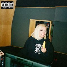 a blonde woman in a black shirt is holding a banana and looking at the camera