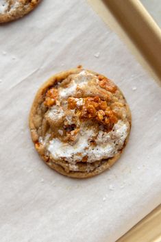 three cookies with white frosting and crumbled toppings sitting on parchment paper