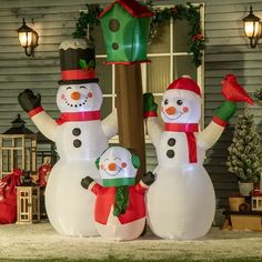 inflatable snowmen are standing next to a christmas tree and birdhouse on the front lawn