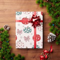 a christmas present wrapped in white paper with red ribbon and decorations around it on a wooden table