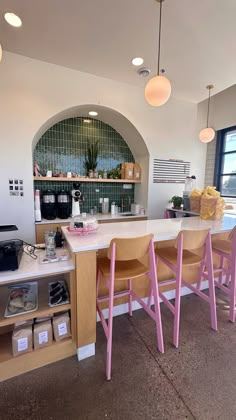 a kitchen with pink stools next to a counter top and shelves on the wall