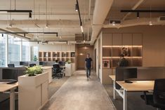 a man walking through an office with lots of desks and planters on the walls