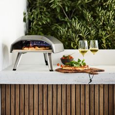 an outdoor pizza oven with two glasses of wine on the counter top next to it