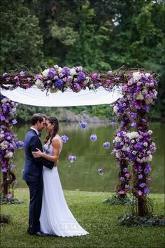 a bride and groom standing under an arch with purple flowers