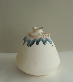 a white vase with blue and orange designs on the top is sitting on a table