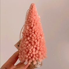 a pink christmas tree ornament is held up by a person's hand