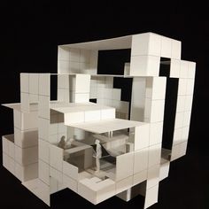 a model of a house made out of white blocks on a black surface with one person standing in the doorway