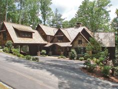 a large house in the woods with lots of trees on both sides and a driveway leading to it