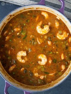 a pot filled with shrimp and vegetables on top of a blue table cloth next to a spoon