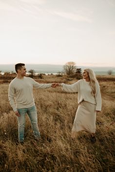 a man and woman holding hands while standing in the middle of a field with tall grass