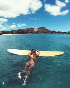 a woman is laying on her surfboard in the ocean with mountains in the background