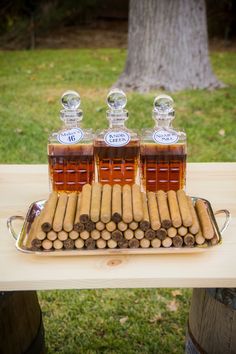 three bottles of liquor and some cigars on a table with grass in the background