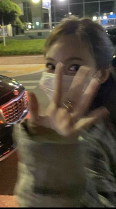 a woman making the vulcan sign with her hand in front of a car at night