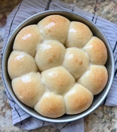 a bowl filled with rolls sitting on top of a counter next to a blue towel