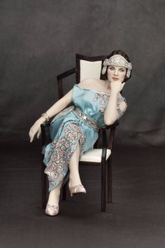 a doll is sitting in a chair with her hand on her chin and wearing a tiara