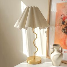 a white vase sitting on top of a table next to a lamp with a beige shade