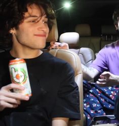 two young men sitting in the back seat of a car, one holding an orange beverage