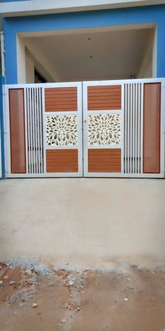 an open gate in front of a blue building with white and brown doors on each side